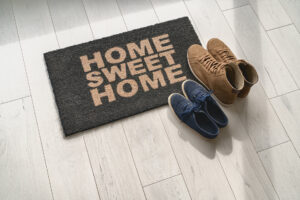 Home Sweet Home Fußmatte am Eingang einer Wohnungstür, darauf steht ein Paar Schuhe